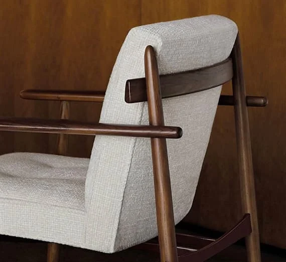 Detailansicht eines modernen Armlehnstuhls mit heller Stoffpolsterung und elegantem Holzgestell in warmem Braunton.