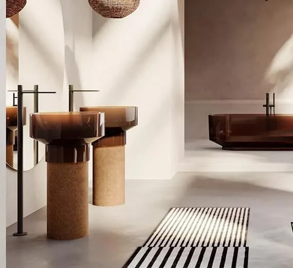 Modernes Badezimmer mit zwei freistehenden Waschbecken aus braunem Glas und Kork, großer Glasbadewanne im Hintergrund und warmem, natürlichem Licht.