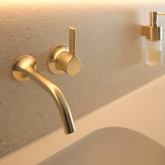 Nahaufnahme eines goldfarbenen Wandarmatur-Wasserhahns im Badezimmer.