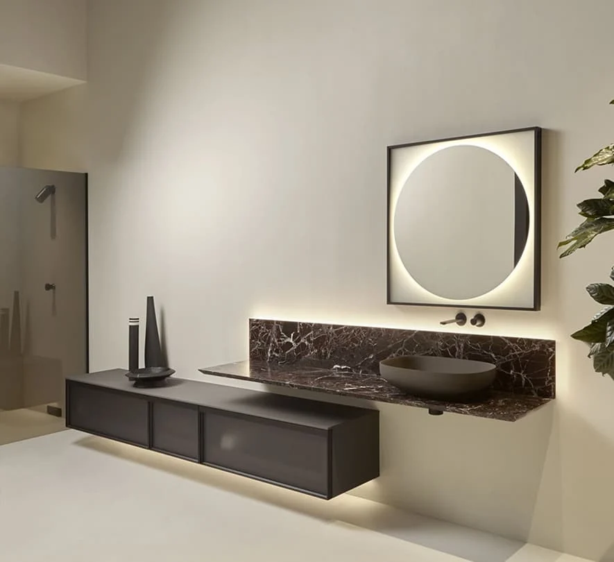 Modernes Badezimmer mit wandhängendem Waschtisch, dunkler Marmorplatte, rundem LED Spiegel und minimalistischer schwarzer Waschschale.