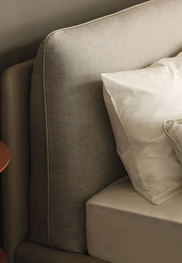 Detailaufnahme eines modernen Bettes mit gepolstertem Kopfteil in Beige und weißen Kissen.