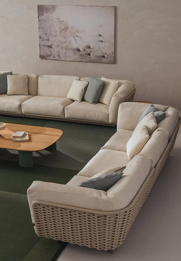 Große, cremefarbene Ecksofa-Landschaft mit geflochtener Rückenlehne, grünen Akzenten und Holz-Couchtisch in modernem Wohnzimmer.