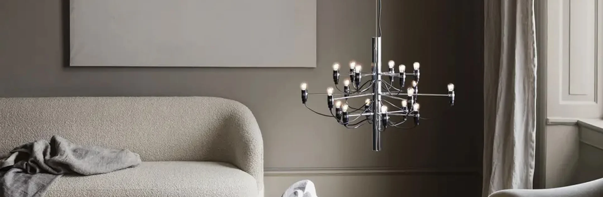 Elegantes Wohnzimmer mit cremefarbenem Sofa, moderner Chrom-Hängeleuchte und minimalistischer Wanddekoration.