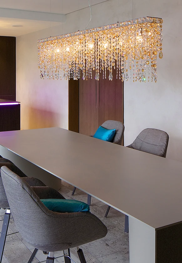 Moderner Essbereich mit langem Tisch, gepolsterten Stühlen und funkelndem Kristallleuchter mit goldenen Akzenten.