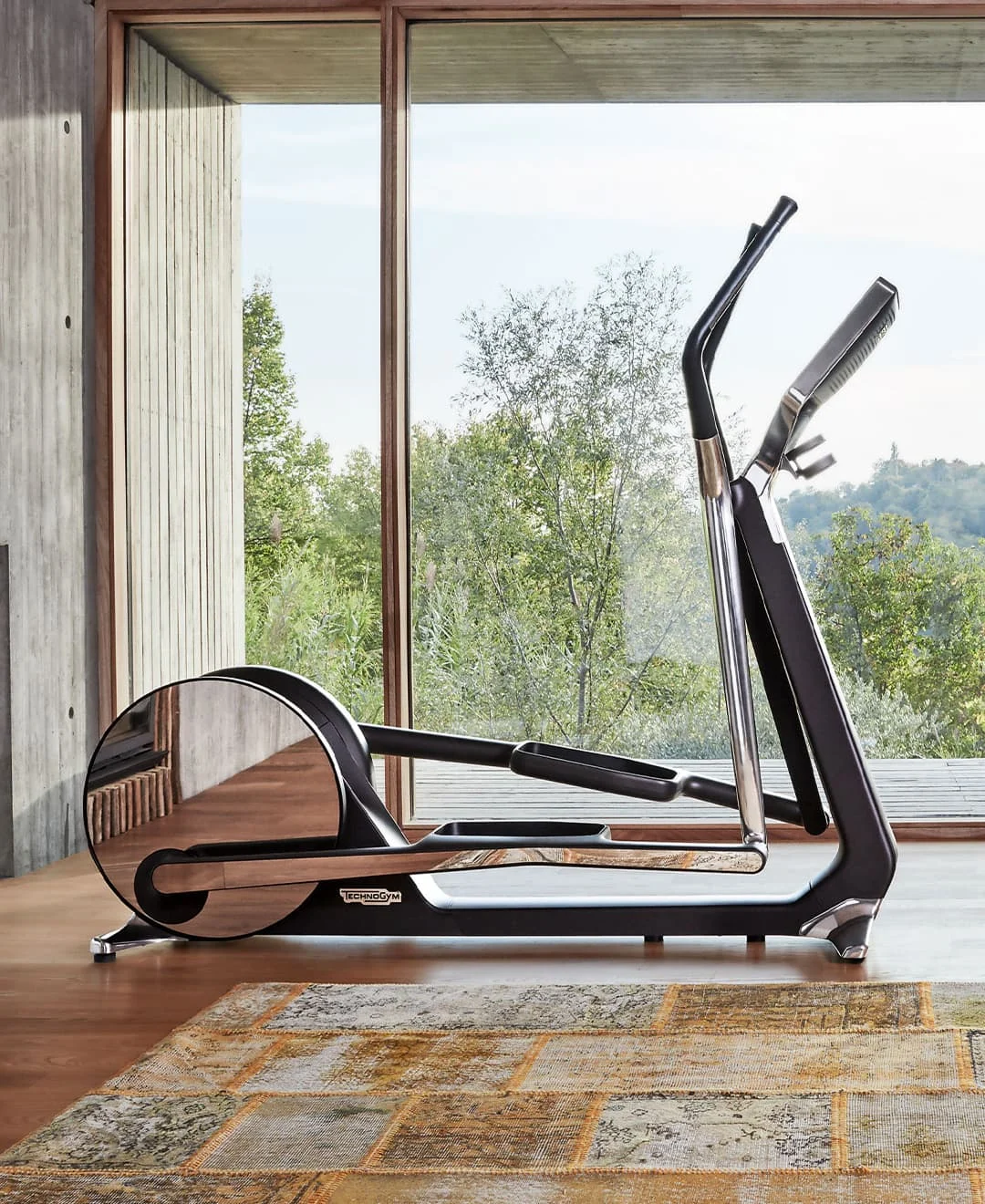 Moderner Crosstrainer in einem hellen Raum mit großer Glasfront und Blick auf eine grüne Landschaft.