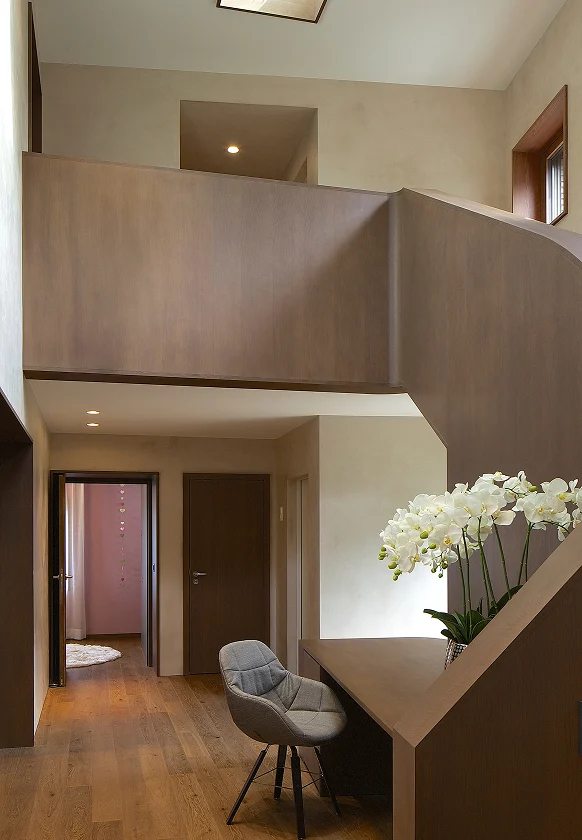 Offener Flur mit skulpturaler Holztreppe, integriertem Schreibtisch und weiß blühenden Orchideen auf dem Tisch.