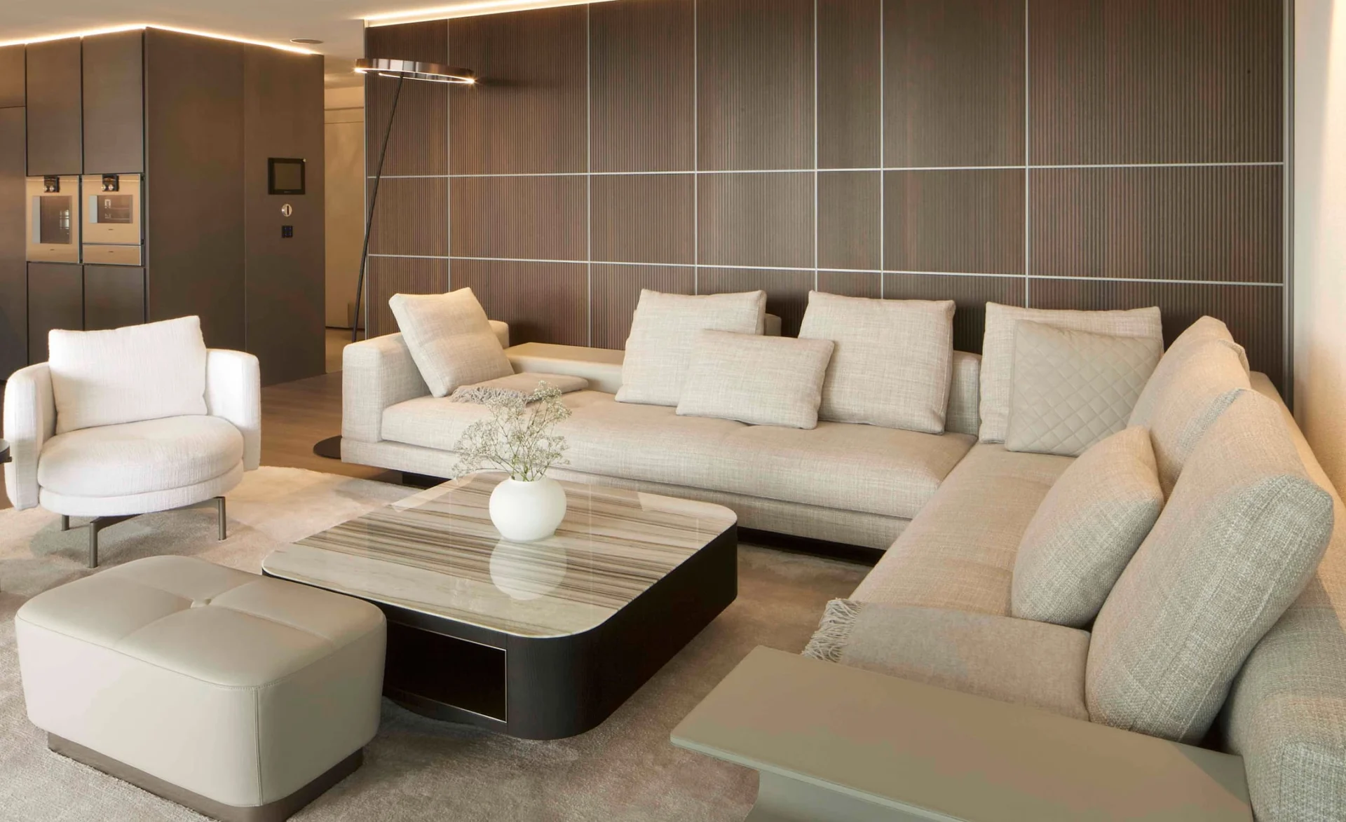 Helles Wohnzimmer mit großer beigefarbener Ecksofa-Landschaft, modernen Sesseln und einem eleganten Couchtisch aus Marmor vor einer holzvertäfelten Wand.