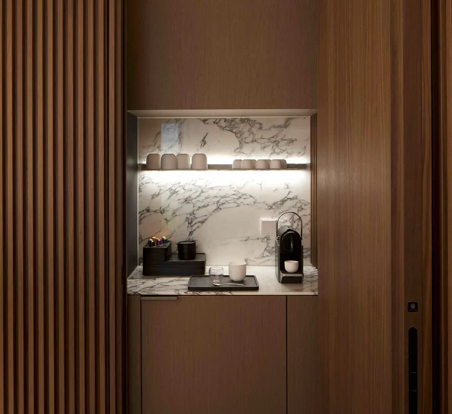 Integrierte Kaffee-Nische mit Marmor-Rückwand, Holzverkleidung, Espressomaschine und stimmungsvoller Beleuchtung im maßgefertigten Küchenmöbel.