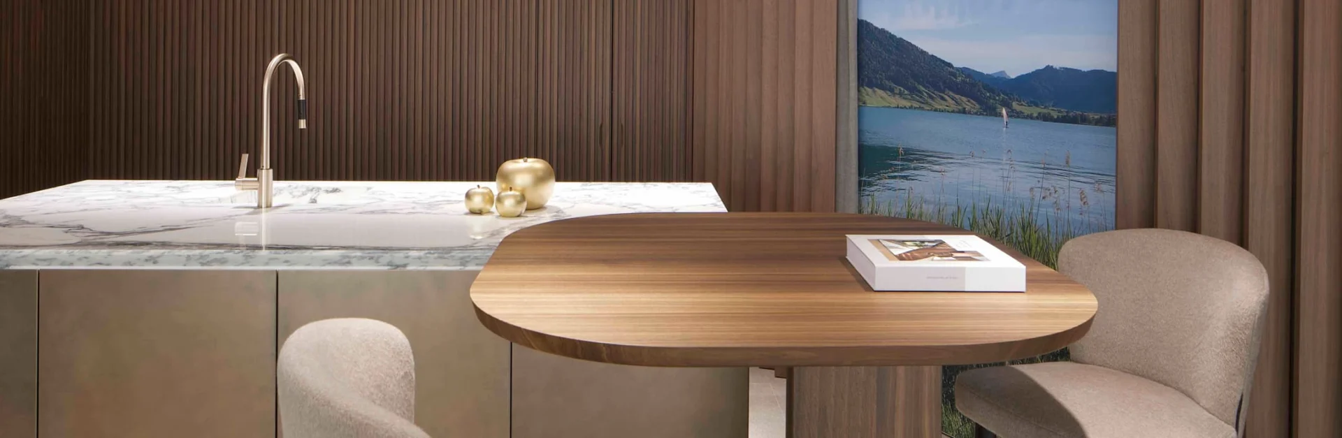 Elegante Kücheninsel mit weißer Marmorplatte, goldenen Dekoelementen und rundem Holztisch vor einer Wand aus Holzlamellen und Seeblick.