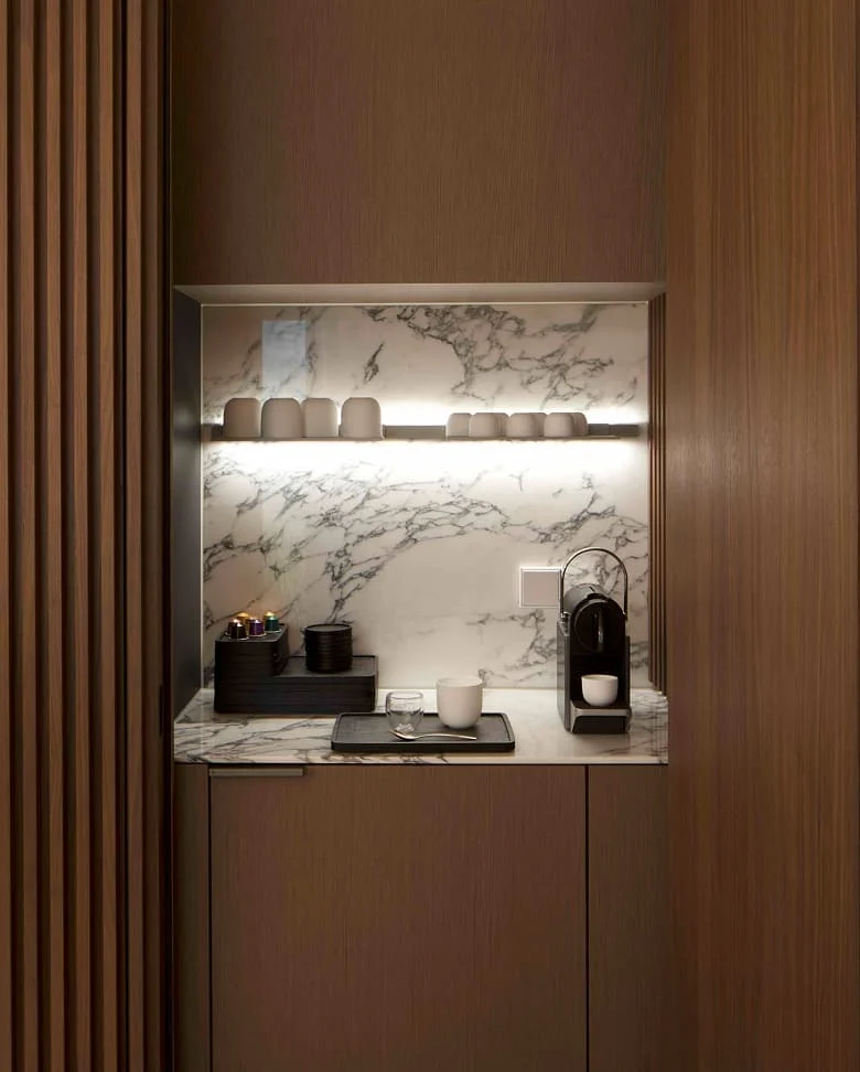 Kompakte Kaffeestation mit Marmorwand, Nespresso-Maschine und offenen Tassenregalen, eingebettet in elegante Holzlamellen im Trendline Showroom.
