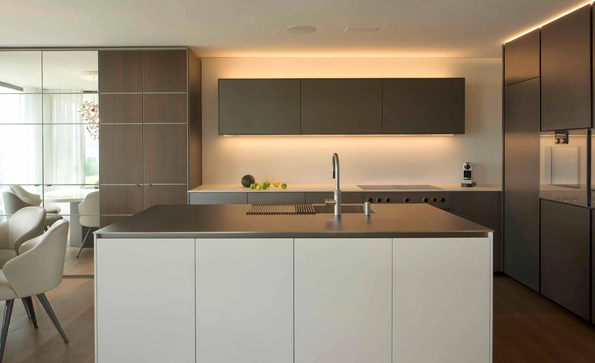 Moderne Designküche mit großer Kochinsel, warmem Licht und eleganten, dunklen Fronten.