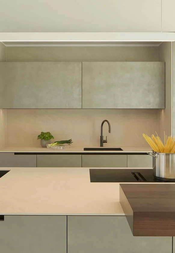 Moderne Küche mit heller Arbeitsplatte, eingelassener Spüle und minimalistischem Oberschrankdesign, mit Kräutern und frischem Gemüse auf der Theke sowie einem Topf mit Spaghetti auf dem Kochfeld.