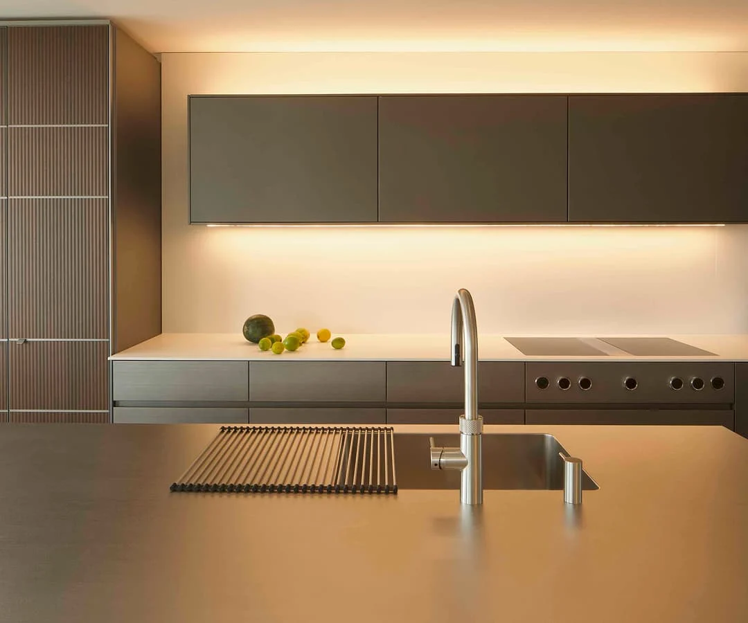 Moderne Küche mit minimalistischen Schränken in warmen Brauntönen und beleuchteter Rückwand mit Eingebauten.