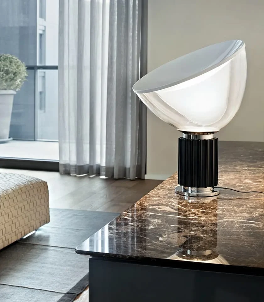 Moderne Tischleuchte auf dunkler Marmorplatte in elegantem Wohnraum mit großen Fenstern.