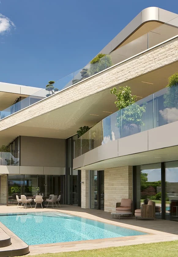 Moderne Villa mit Glasfassade, Balkonterrassen und Pool im Garten bei sonnigem Himmel.