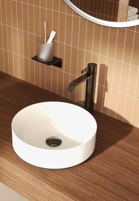 Modernes Badezimmer mit rundem Aufsatzwaschbecken, dunkler Armatur und warmen Wandfliesen über einer Holzoberfläche.