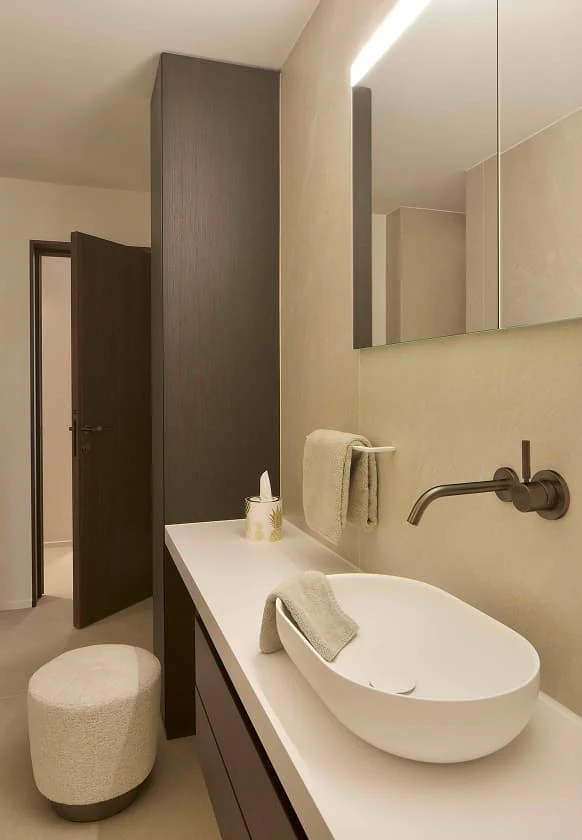 Modernes Badezimmer mit freistehendem Waschbecken, wandmontierter Armatur und heller Steinwand.