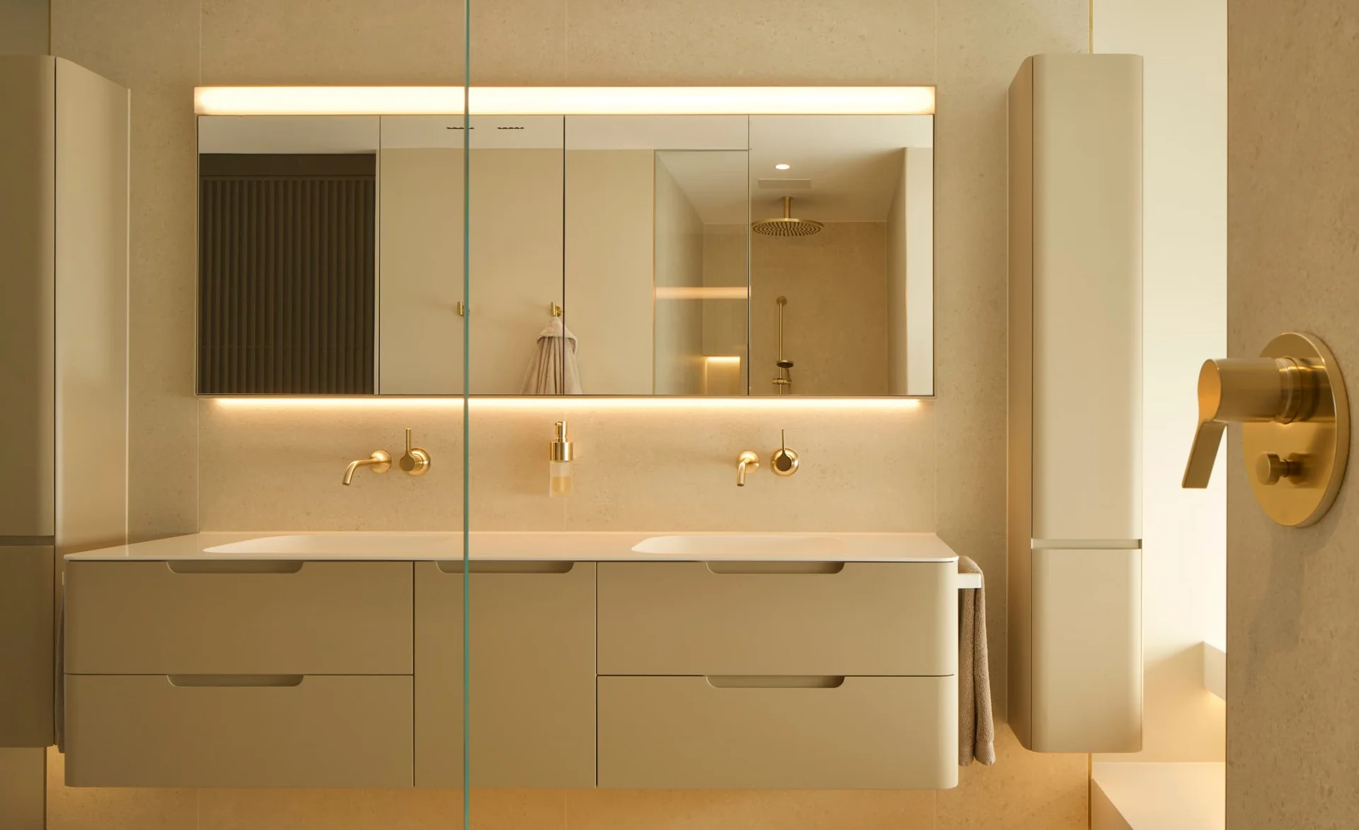 Helles modernes Badezimmer mit Doppelwaschbecken, goldenen Armaturen, großen Spiegelschränken und indirekter Beleuchtung.