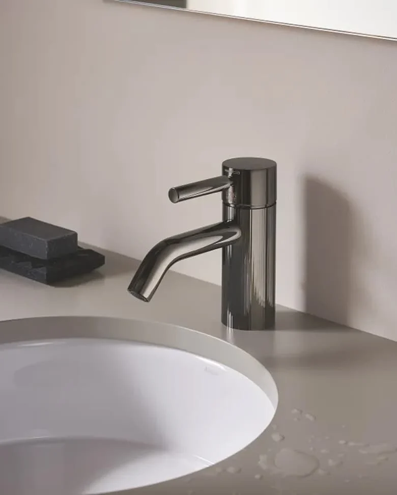 Modernes Badezimmer mit dunklen Natursteinfliesen, rundem Waschbecken und beleuchtetem Spiegel, Blick in begehbaren Schrankraum.