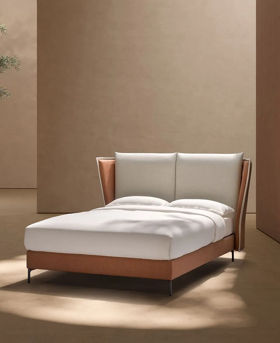 Modernes Doppelbett mit hohem, weich gepolstertem Kopfteil und seitlichen Flügeln, bezogen in Beige und Terrakotta, in einem minimalistischen Raum mit warmen Naturtönen.