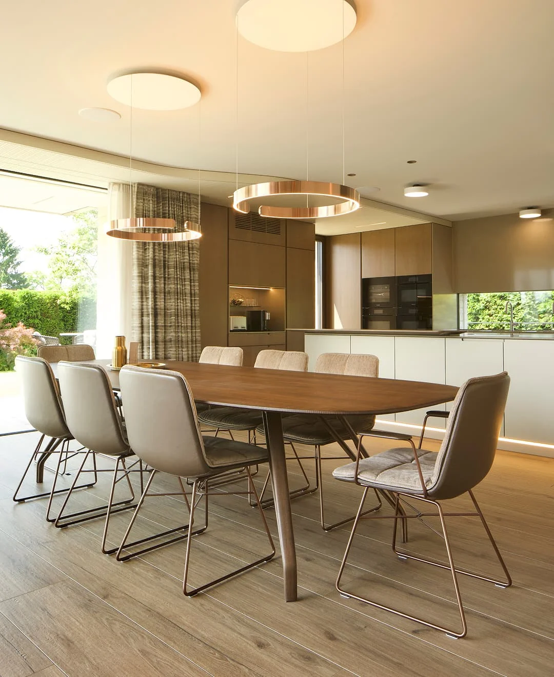 Modernes Esszimmer mit großem Holztisch, eleganten Stühlen und offenen Blick in die hochwertige Küche.