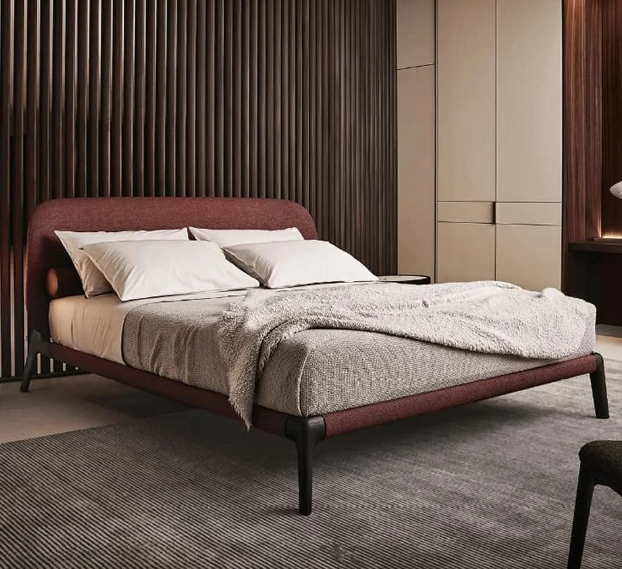 Modernes Schlafzimmer mit einem eleganten Polsterbett in warmem Rotton, weicher Bettwäsche, dunkler Holzlamellenwand und eingebautem Schrank.