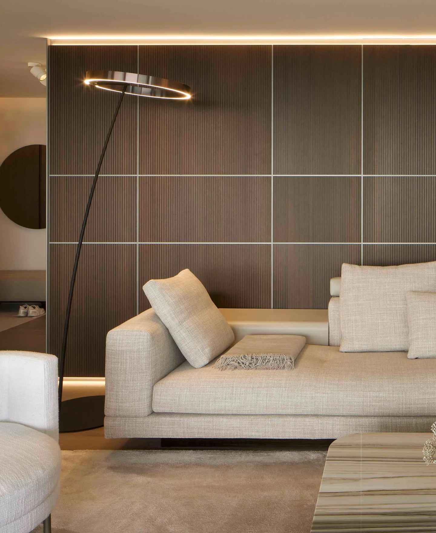 Modern living room with beige sofa, slim ring floor lamp and wall-high wood panel with fine lines.