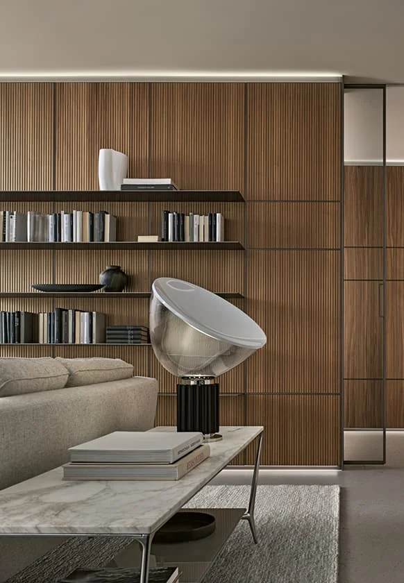 Modernes Wohnzimmer mit Holzlamellenwand, offenen schwarzen Regalen, dekorativen Büchern und einer Designer-Tischlampe auf einem Marmortisch.