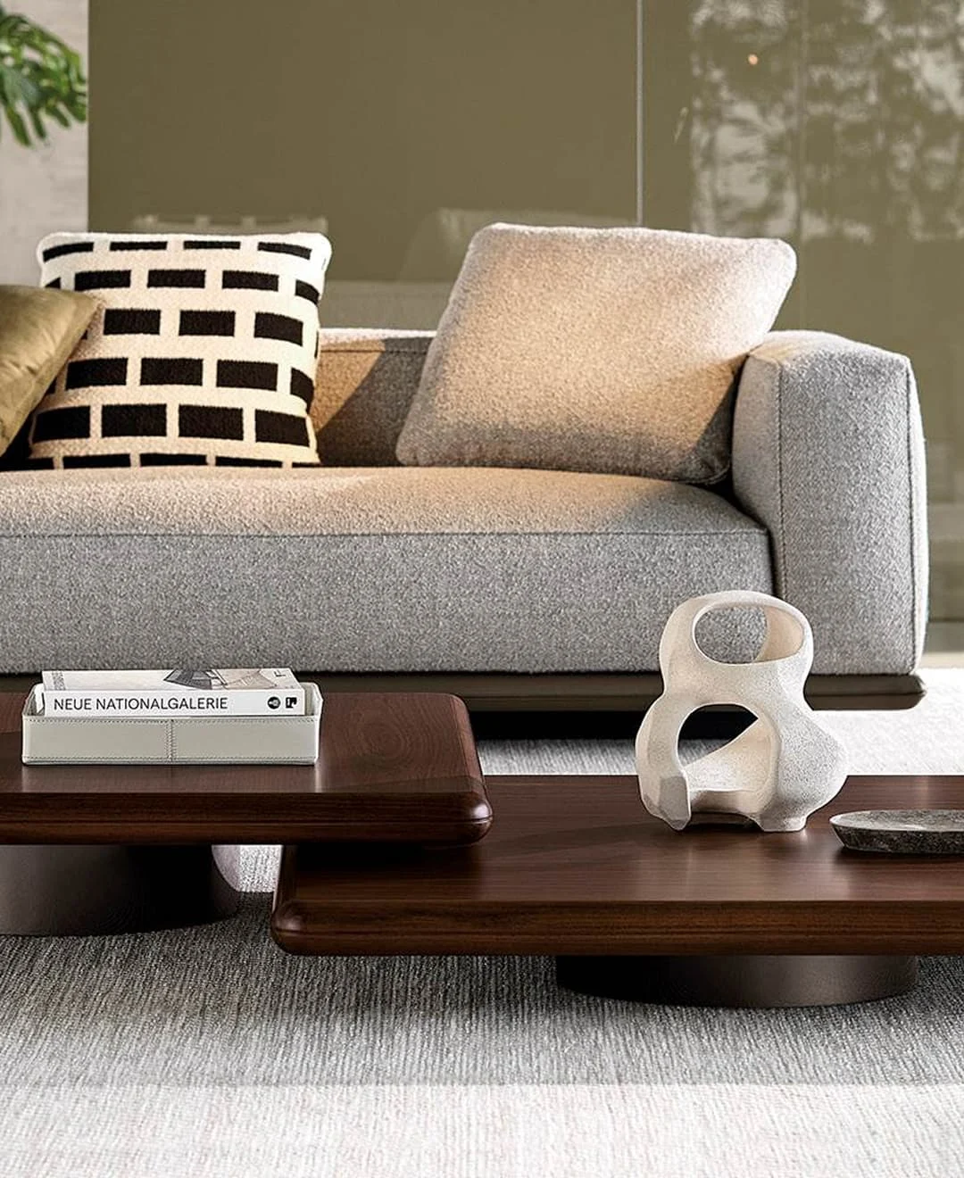 Modernes Wohnzimmer mit hellgrauem Sofa, dekorativem Kissen und zwei niedrigen Holztischen mit Kunstobjekt und Buch.