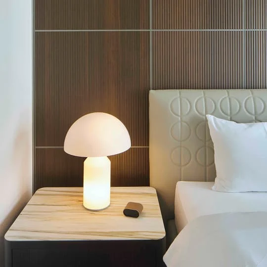 Nachttisch mit runder Tischlampe und modernem, gepolstertem Kopfteil vor einer Wand aus Holzpaneelen.