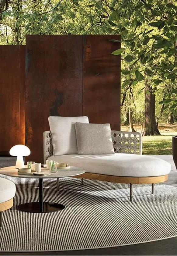 Elegante Outdoor-Lounge mit heller Polsterliege, rundem Beistelltisch und moderner Gartenkulisse im Grünen.