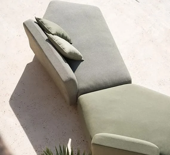 Modernes Outdoor-Loungeelement in hellgrün mit zwei passenden Kissen auf hellem Steinboden.