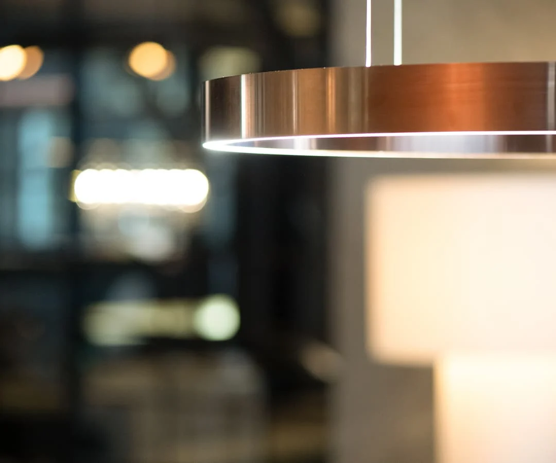 Detailaufnahme einer modernen, ringförmigen Pendelleuchte aus Metall mit warmem Licht in elegantem Innenraum.
