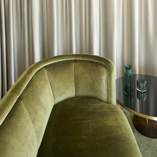 Grünes Samtsofa mit Glas-Beistelltisch und dekorativen Gläsern.