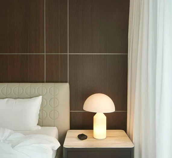 Modernes Schlafzimmer mit gepolstertem Bettkopfteil, Designer-Tischlampe auf einem Beistelltisch und eleganten Holzpaneelen im Trendline Showroom.