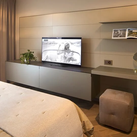 Modernes Schlafzimmer mit TV-Wand, integriertem Sideboard und Schreibtisch.