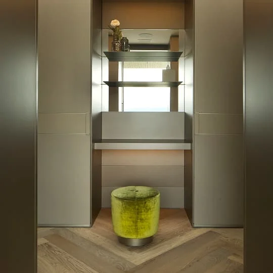 Eleganter Schminkbereich mit Spiegel, Regalen und grünem Hocker.