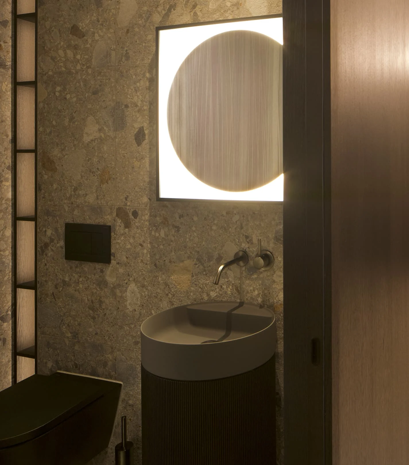 Elegantes Gäste-WC mit dunklem Steinboden, modernem Waschtisch, wandhängender Armatur und hinterleuchtetem rundem Spiegel – stilvolles Beispiel für hochwertige Designmarken im Interior-Bereich.