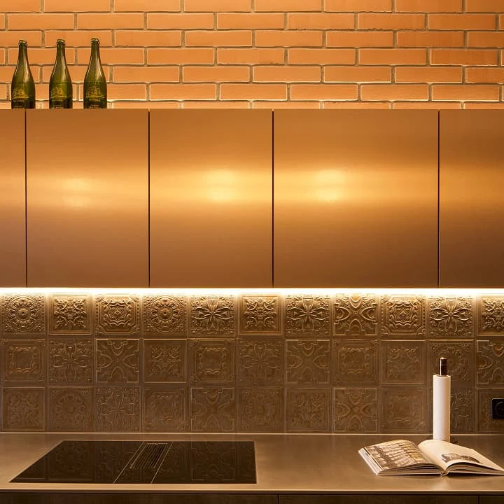 Moderne Küche mit goldenen Fronten, dekorativer Fliesenrückwand und warmer LED-Beleuchtung – stilvolles Design mit edlen Materialien und harmonischer Lichtstimmung.