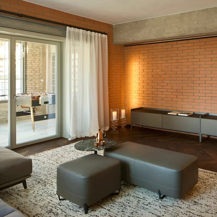 Gemütliches Wohnzimmer mit Backsteinwand, modernen Sitzmöbeln und bodenlangen Vorhängen – stilvolles Loft-Ambiente mit warmem Licht und elegantem Design.