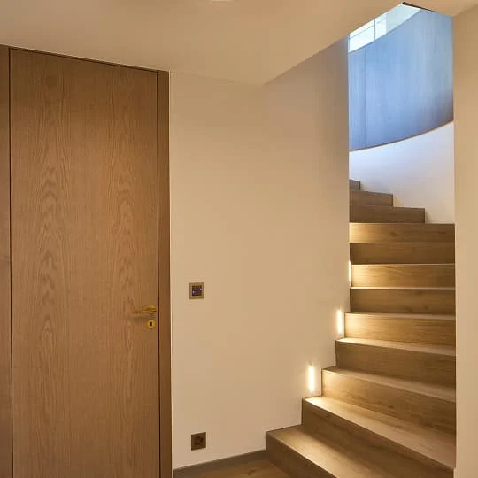 Warm beleuchtetes Treppenhaus mit Holzstufen und weißer Wand.