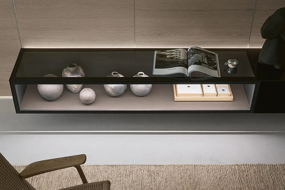 Moderne Wandkonsole mit Glasoberfläche, dekorativen Keramikvasen im unteren Fach und offenem Bildband auf der Ablage.