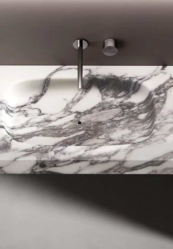 Detailansicht eines integrierten Waschtischs aus weißem Marmor mit grauer Maserung und minimalistischer Wandarmatur in modernem Badezimmerdesign.