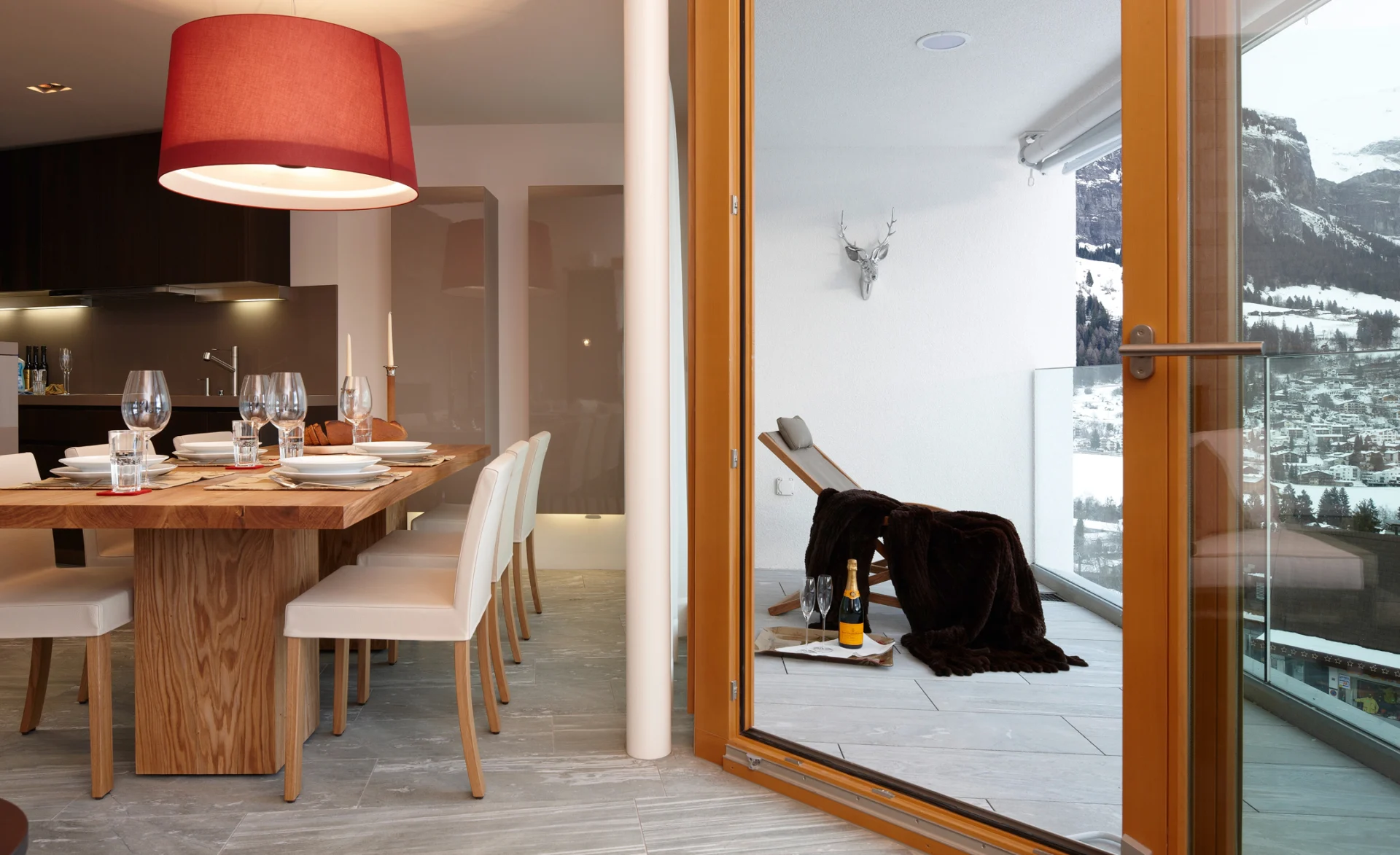 Moderner Wohnbereich mit großem Holzesstisch, heller Beleuchtung und Blick auf den verschneiten Balkon.