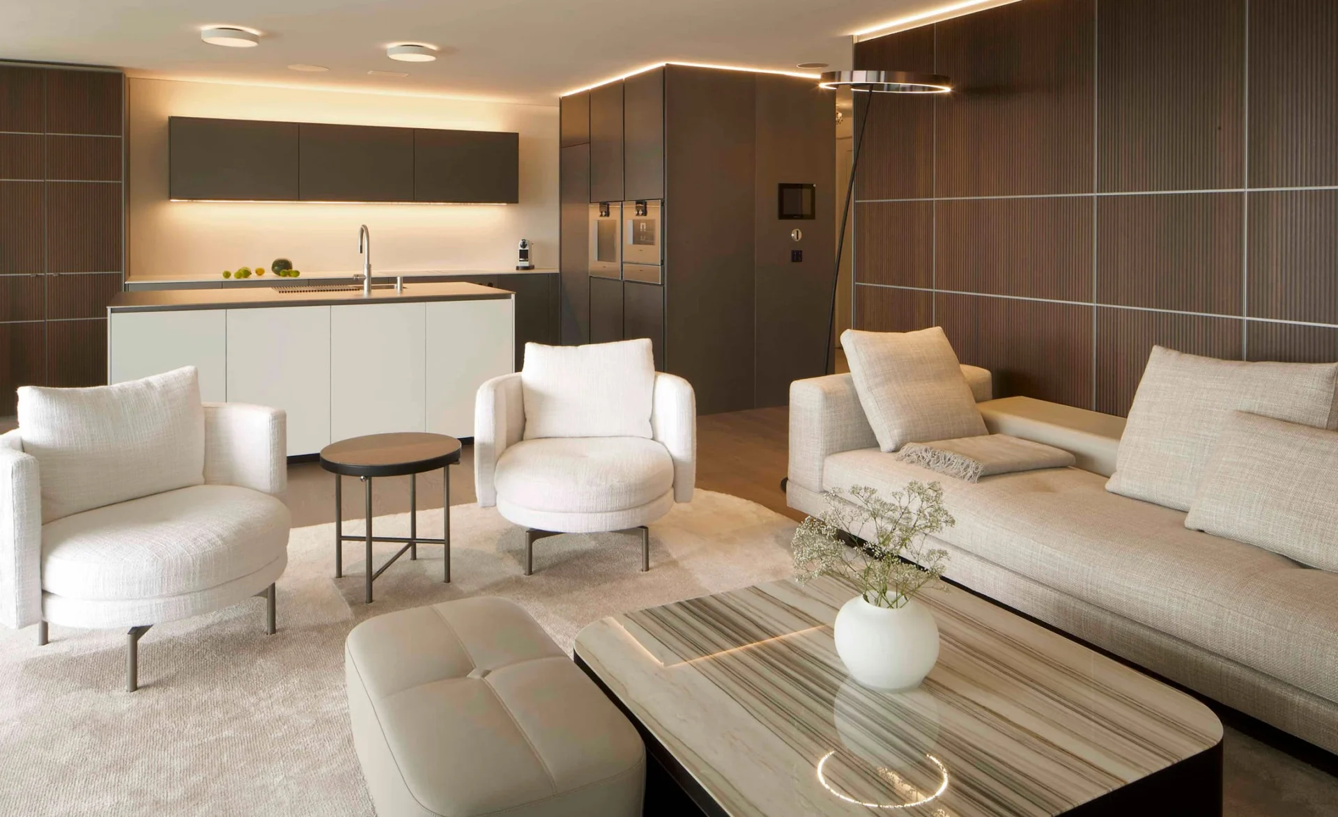 Helles Wohnzimmer mit moderner offener Küche, cremefarbenen Polstermöbeln und stilvoller Holzverkleidung an der Wand.